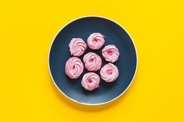 Appetizing pink desserts on a bright blue plate on yellow background with copy space. Flat lay.