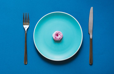 Flat lay  - Delicious and fresh sweet desserts on color plate with fork and knife on blue background. Handmade pink marshmallows.