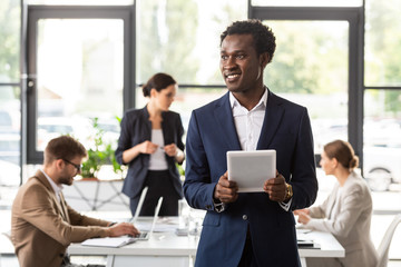 smiling african american businessman in formal wear holding digital tablet in office