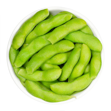 Edamame, green soybeans in the pod, in white bowl. Unripe soya beans, also Maodou. Glycine max, a legume, edible after cooking and rich protein source. Closeup, on white background, macro food photo.