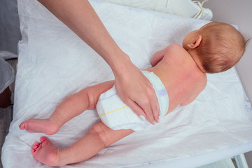 caucasian mother applying baby powder before putting diapers on her four month old baby in bed at home