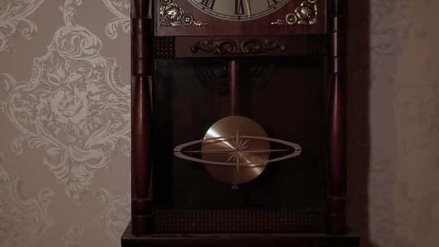 Close up of an old wall hanged clock with the pendulum swinging forth and back. Filmed in slow motion, no camera movements.