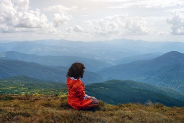 Naklejka na ściany i meble Yoga woman sit in lotus pose on mountain peak. Woman tourist practices yoga and meditates on the mountain. Resting on the highest hill.