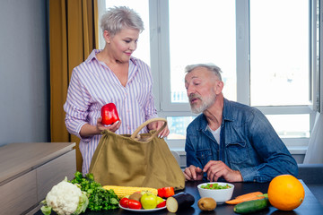 happy elderly man and woman unpacking fruit and peper from cotton eco bag