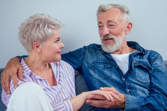 Mature Good-looking Well Dressed Couple Sitting In Sofa In Day Light From Big Window And Yellow Curtains In Living Room,touching Hand