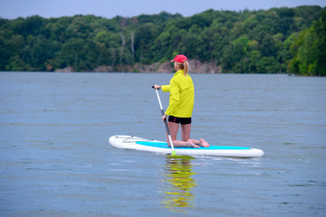 Fototapeta na wymiar SUP Stand up paddle board concept - young woman paddle boarding on a lake