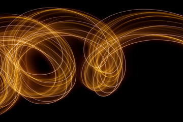 Long exposure photograph of metallic gold neon colour in an abstract swirl, parallel lines pattern against a black background. Light painting photography.