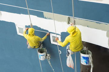painters hanging on roll, painting color on building wall.