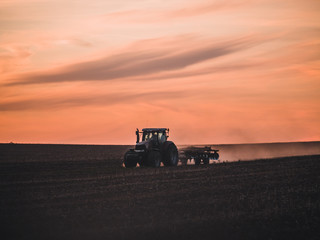 Fototapeta premium Tractor on filed by sunset.