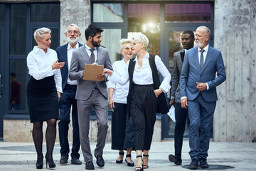 Group of businessmen dressed in stylish office clothes discuss project and move in street