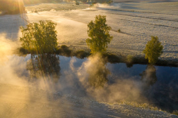 Autumn foggy nature landscape aerial view. Beautiful sunny october morning on river side. Trees in sunlight. Fall. Misty nature with sunbeams from above