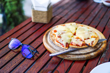 The pizza on the table is being cut by a knife and black glasses are placed near.