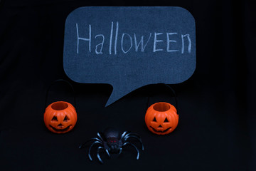 Baskets in the form of pumpkins for collecting sweets, a large black spider and the inscription in chalk "Halloween". Halloween decoration