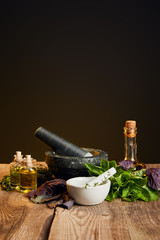 mortars with pestles and bottles with oil near fresh herbs on wooden table isolated on black