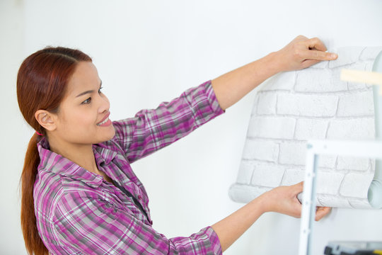 woman applying wallpaper on wall in new house