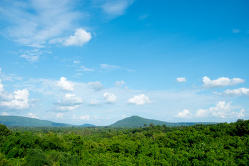 Mountains covered forest, trees and blue sky with clouds.
