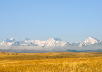 autumn prairie with dry grass and snowbound mountain chain in a mist beyond