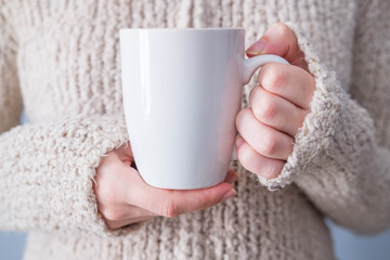 Girl in a warm cardigan is holding white mug