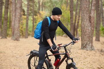 Close up portrait of biker riding on his bike in autumn or spring inspirational forest landscape, handsome young man cycling on road in woods. Sport, active recreation and inspiration concept.