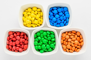 Five squared bowls with small red, blue, green and orange coated chocolate candies similar to m&ms...