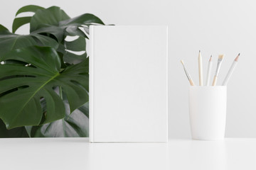 White book mockup with workspace accessories and a monstera plant.
