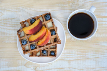Chocolate Belgian waffles with fruits and cup of coffee on white wooden background. Delicious breakfast. Top view