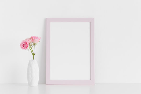 Pink frame mockup with pink roses in a vase on a white table.Portrait orientation.