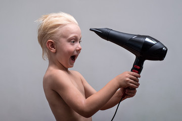 Blond boy with wet hair is funny dried by a hairdryer. White background