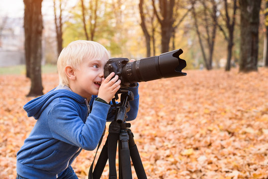 Little blond boy takes pictures on a SLR camera. Autumn Park