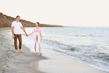 Young married couple walks along the sea coast. Pregnancy. Pre-sunset time