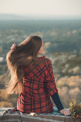 Young woman straightens a long hair sits on a hill overlooking the village. Back view