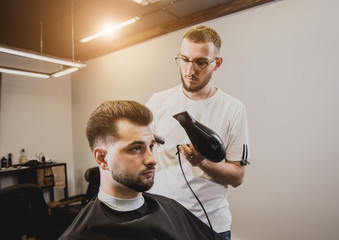 Young man with trendy haircut at barber shop. Barber does the hairstyle and beard trim.