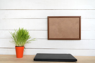 Empty frame on white wall. Closed notebook and green houseplant. Home workplace. Place for text