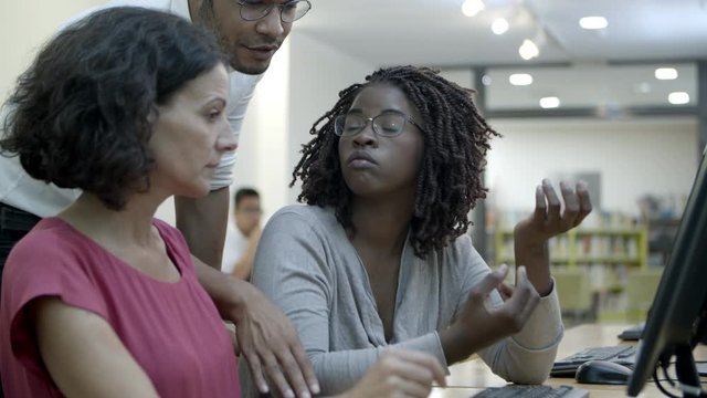 Thoughtful students discussing project in public library. Group of people talking and pointing at screen. Education concept