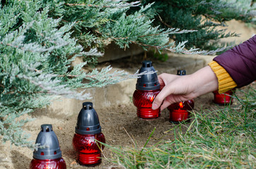 Women put a red candle to a tombstone covered by pine - all souls day preparing in the cemetery - Powered by Adobe