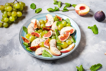 Fresh fruit and berry salad with grapes, fig and peach on concrete background. Healthy food.