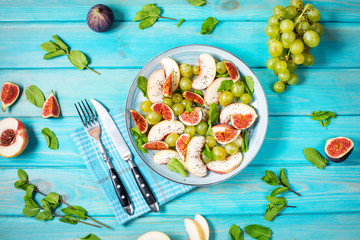 Fresh fruit and berry salad with grapes, fig and peach on blue wooden background. Healthy food.