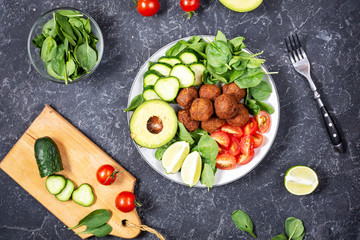 Salad with avocado, falafel, cucumber, cherry tomato and spinach on black stone background.