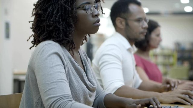Focused African American woman typing on keyboard. Closeup shot of people sitting at tables and typing. Technology concept