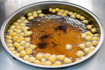 Small donuts being deep fried in boiling oil in a large pan, at a street food market, selective focus