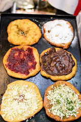 Six donuts called langos, typical Hungarian food specialty, with white cheese, jam, chocolate and sugar on an iron sheet, deep fried dough in direct sunlight, available for sale at a food market