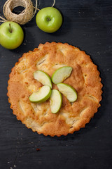 Charlotte apple pie on a black wooden table with slices of green apples. Top view.