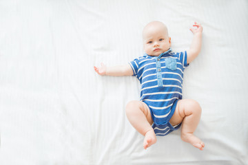 Calm curious baby lying on blue background, looking at camera, top view