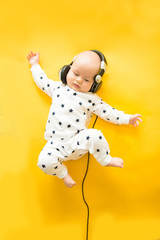 Baby with headphone lies on yellow background