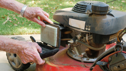 Male landscaper replacing air filter on gas powered lawn mower. Checking air cleaner filter for...