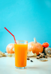 glass of pumpkin juice with a straw on a blue background, pumpkins in the background, vegetable juice