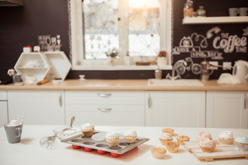 Preparation of brown cupcakes with white cream on the table of modern kitchen