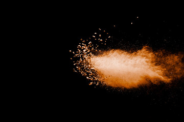 Split debris of stone exploding with orange powder against black background.