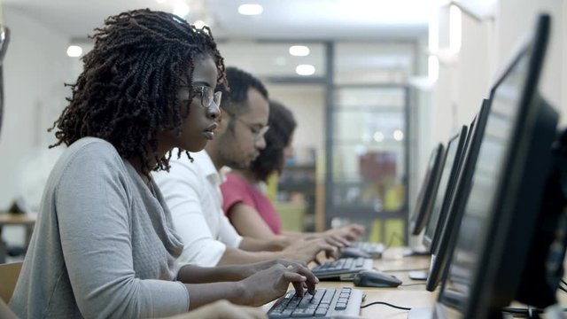 Students passing exams by computers in class. Side view of people sitting at tables and working with computers. Technology concept
