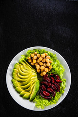 Vegetable salad with chickpea, avocado and red beans in bowl on black stone